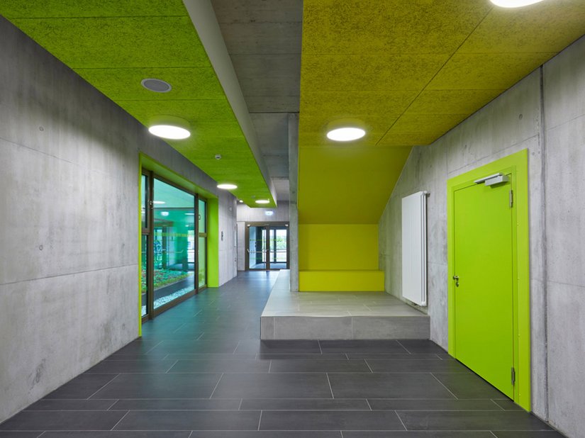 Powierzchnie betonu licowego z kolorowymi akcentami w różnych odcieniach zielonego i żółtego tworzą przejrzystą i tętniącą życiem atmosferę.