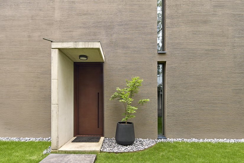 Ciemne, drewniane okna wtapiają się w kompozycję, podczas gdy masywne drzwi ze stali kortenowskiej stanowią wyrazisty akcent.